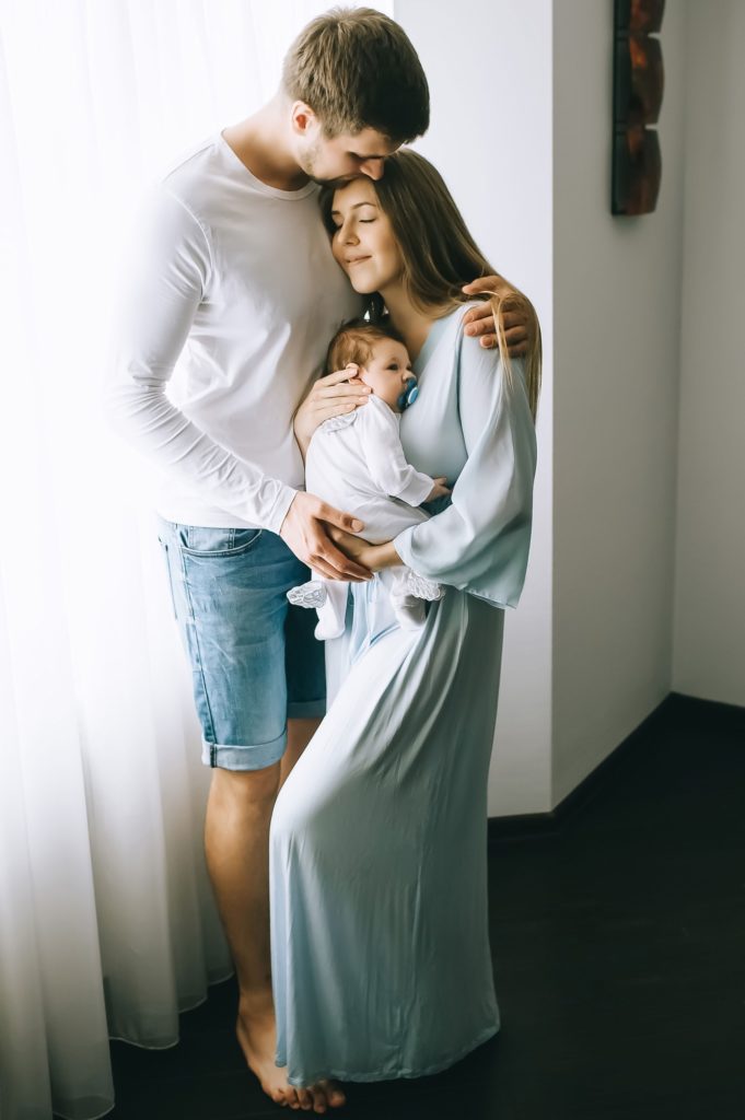 happy family carrying little baby boy in front of curtains at home